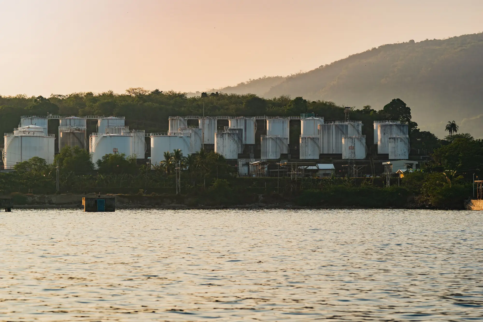 White storage tanks of a waterfront terminal at dusk, seen from across the water